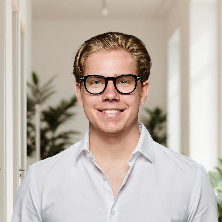 Ein Mann mit Brille und weißem Hemd steht in einem hellen Raum mit Pflanzen.