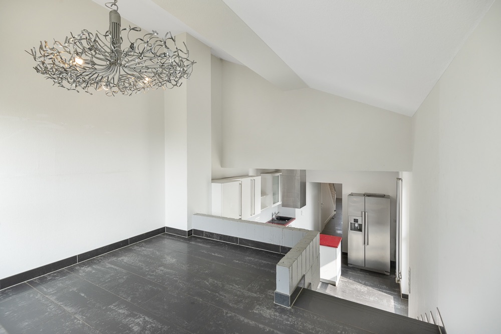 Moderner, heller Wohnraum mit Kronleuchter und Blick auf eine offene Küche mit Edelstahlkühlschrank.