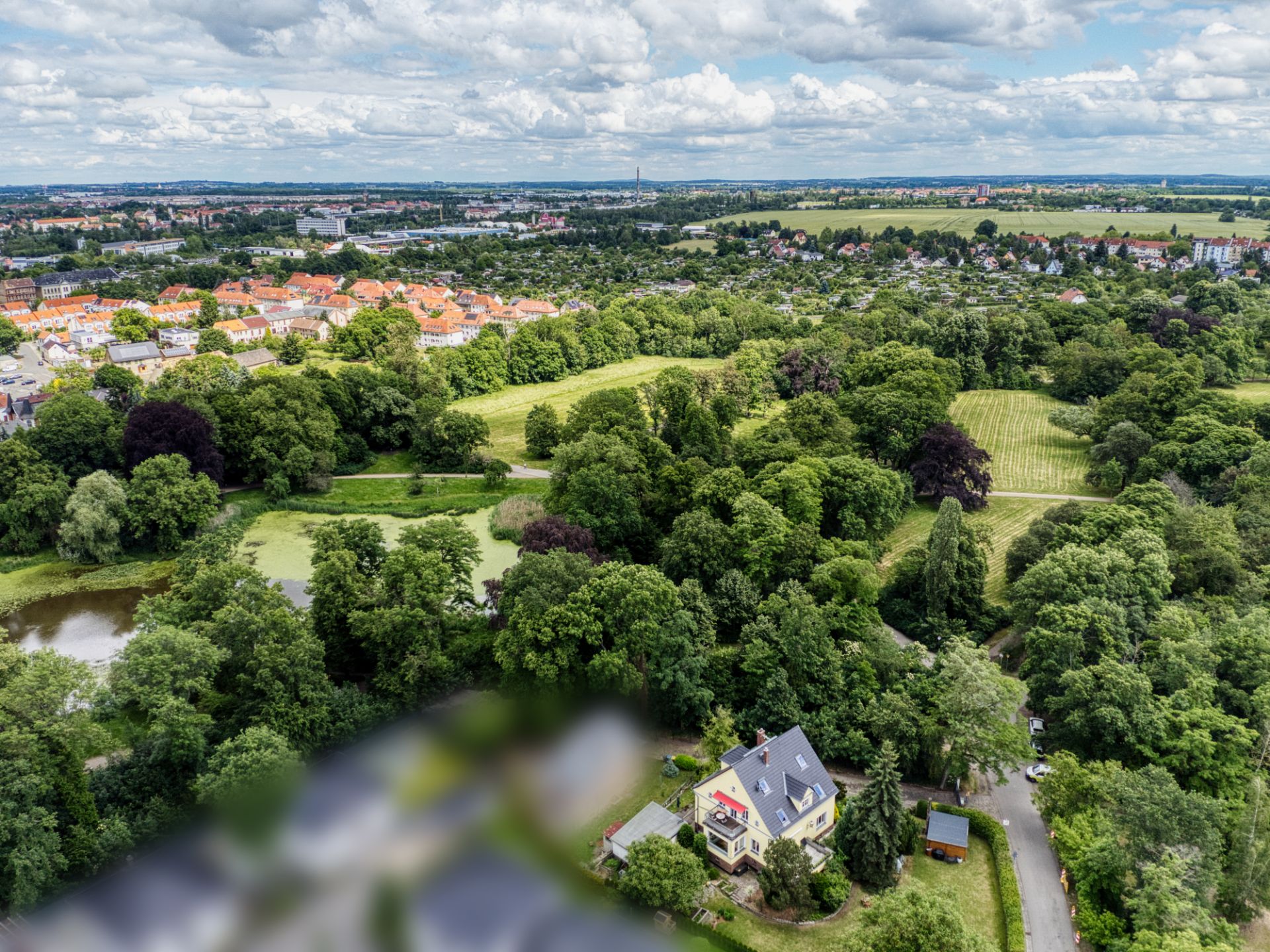 Luftaufnahme eines Wohngebiets mit viel Grün und einzelnen Häusern am Waldrand.