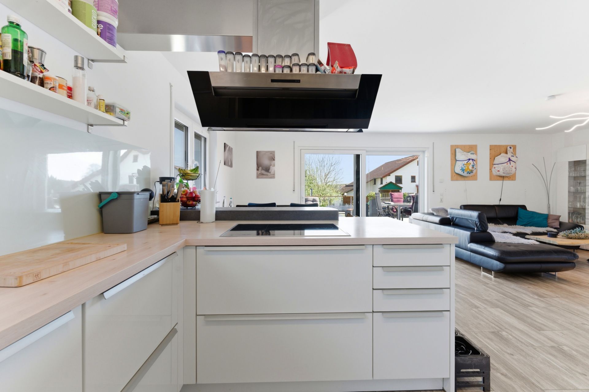Moderne offene Küche mit Insel, Blick ins helle Wohnzimmer mit Sofa und Wandbildern.