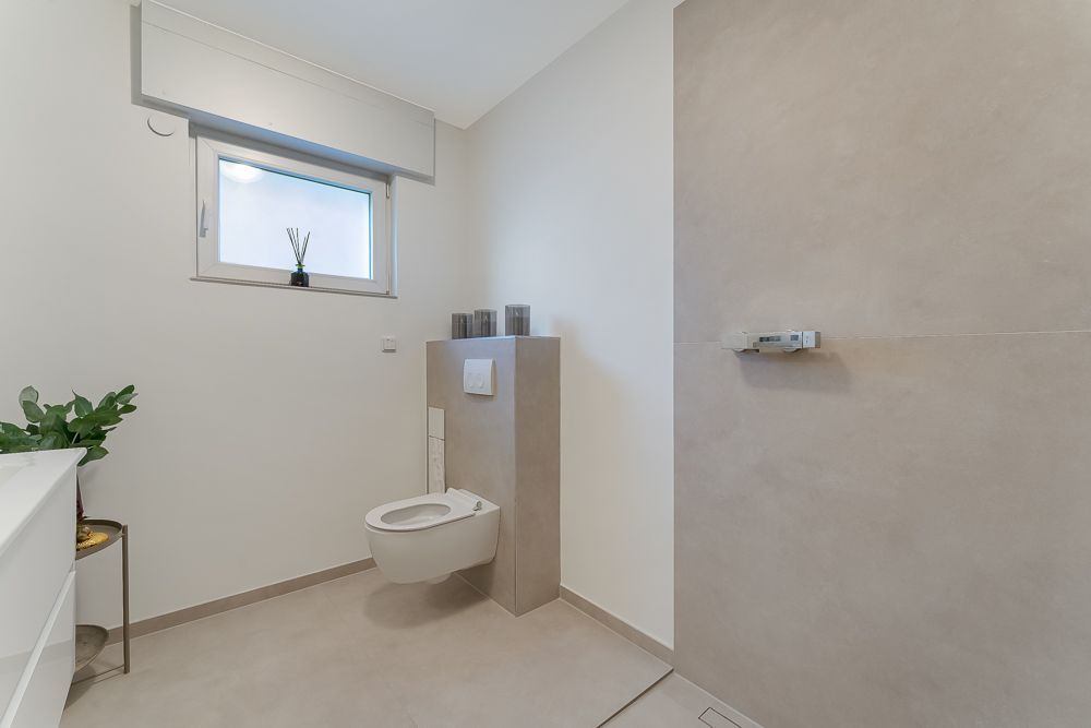 Modernes Badezimmer mit wandhängender Toilette, beiger Dusche und kleinem Fenster.