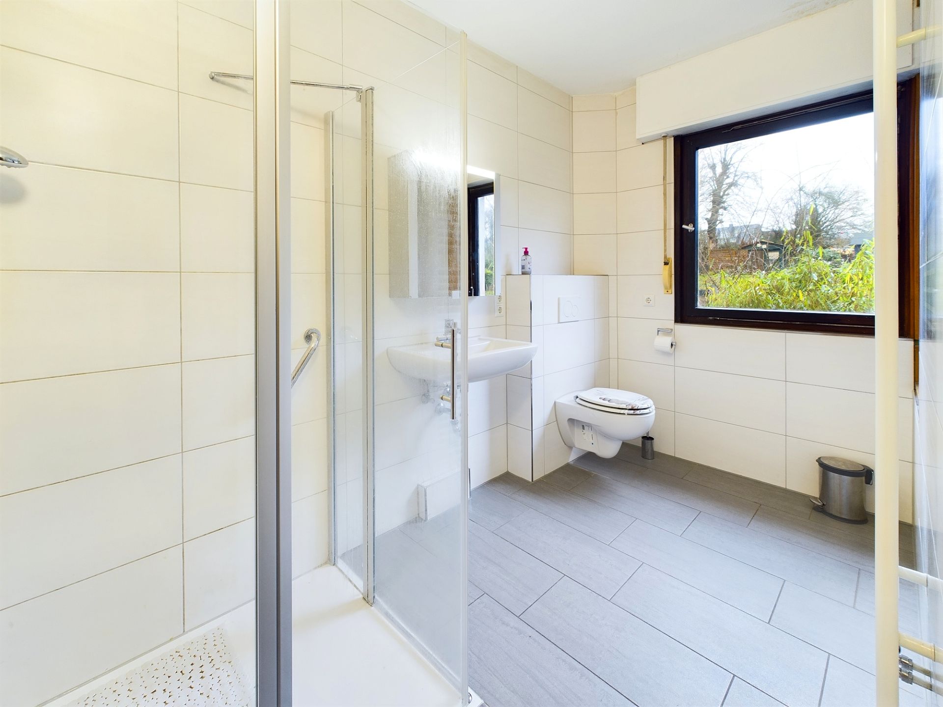 Modernes, helles Badezimmer mit Dusche, Waschbecken und WC, großes Fenster mit Ausblick.
