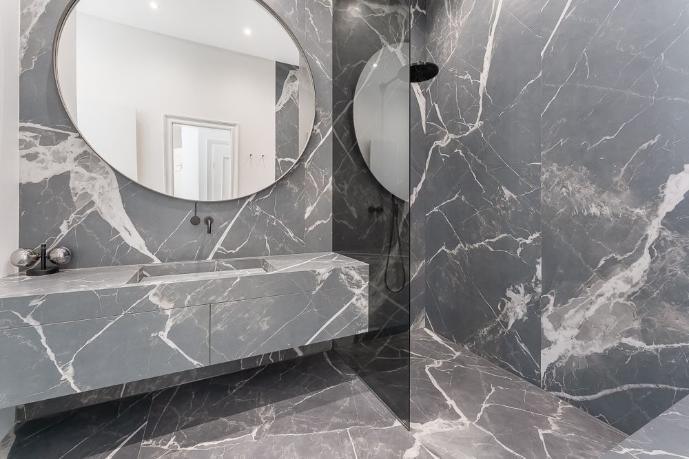 Modernes Badezimmer mit grauen Marmorfliesen, großem runden Spiegel und Doppelwaschbecken.