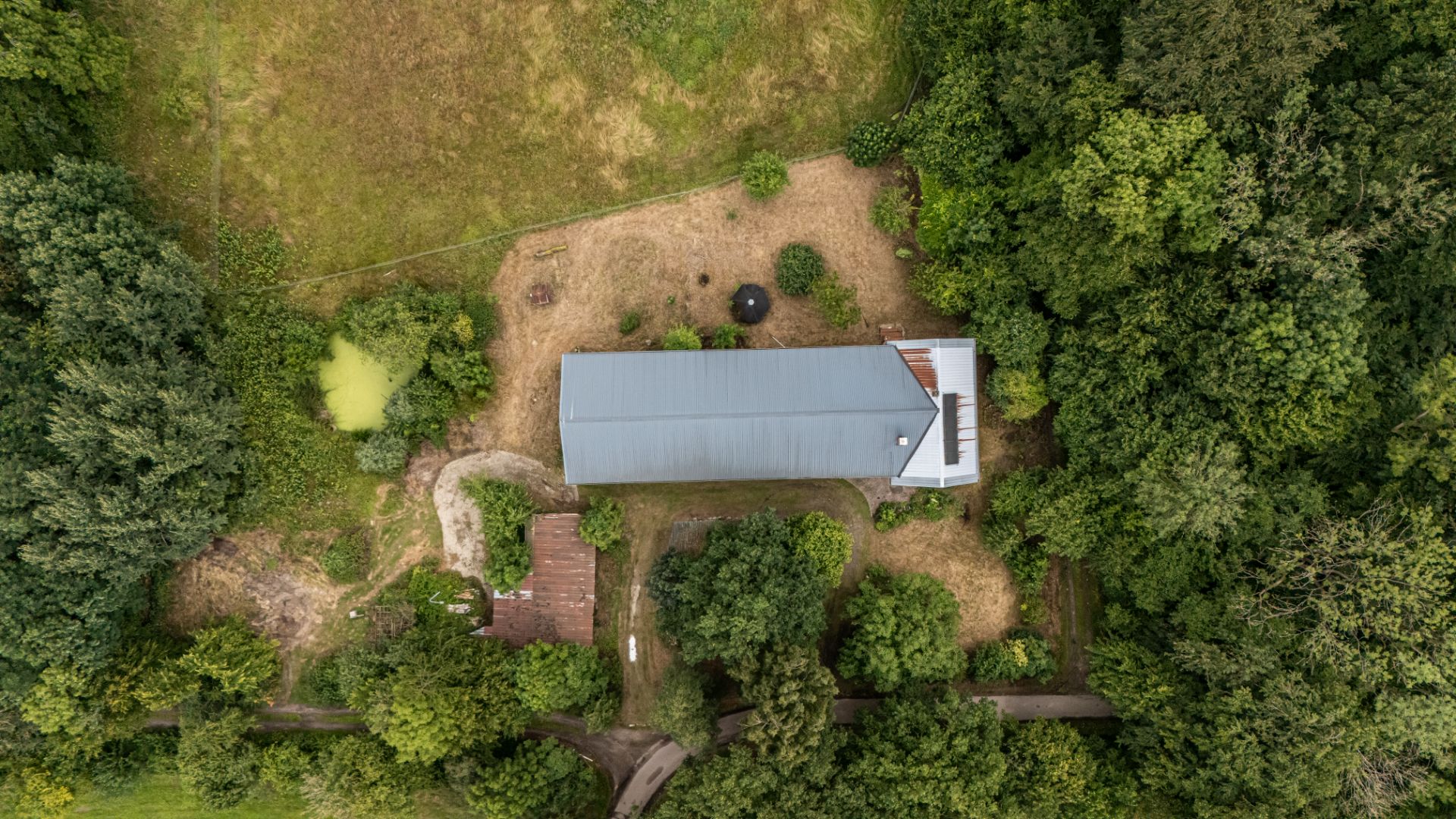 Luftaufnahme eines langen Hauses mit Garten und Bäumen, umgeben von viel Grün.