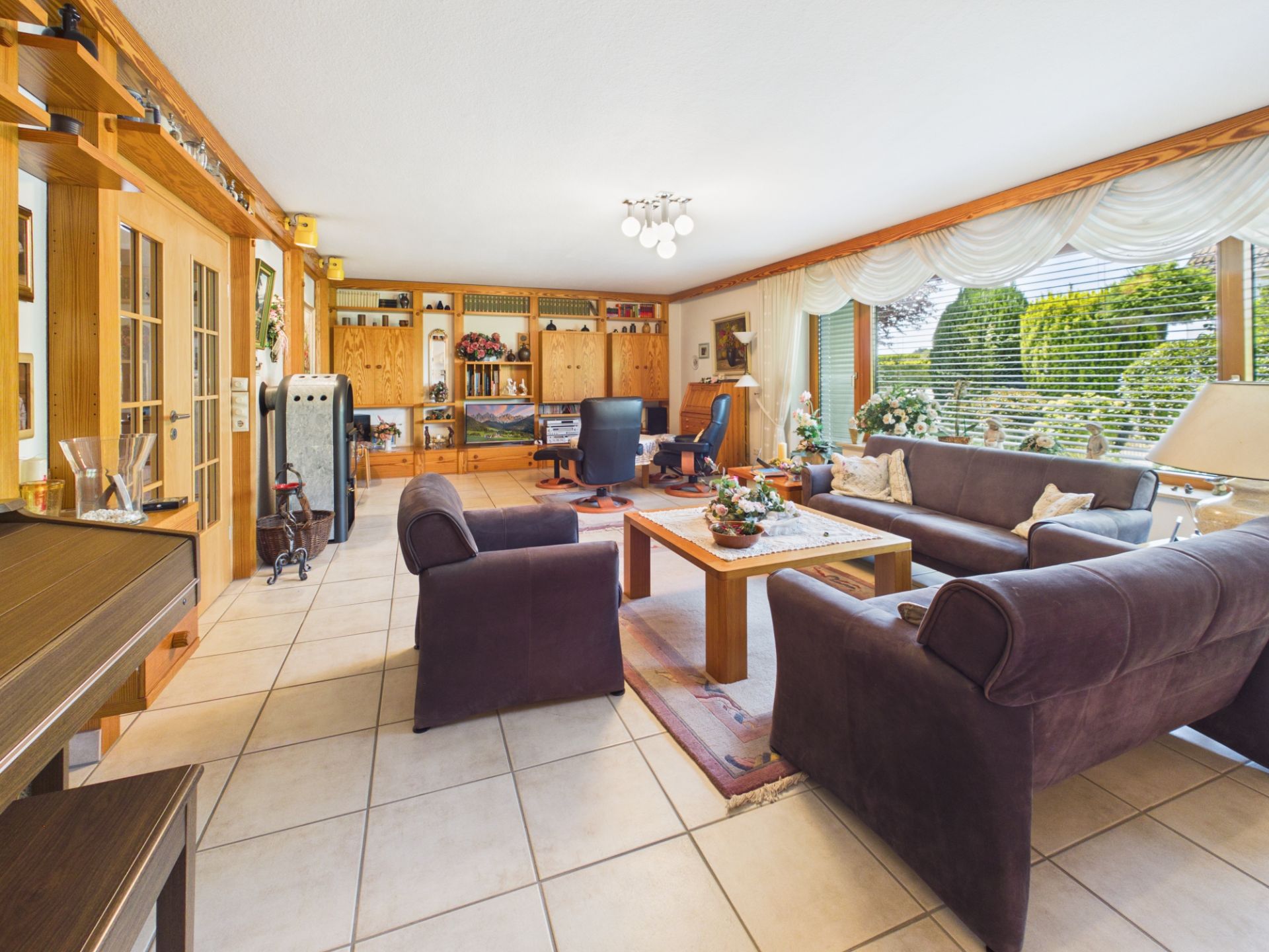 Helles Wohnzimmer mit braunen Sofas, Holzmöbeln, großem Fenster und Fliesenboden.