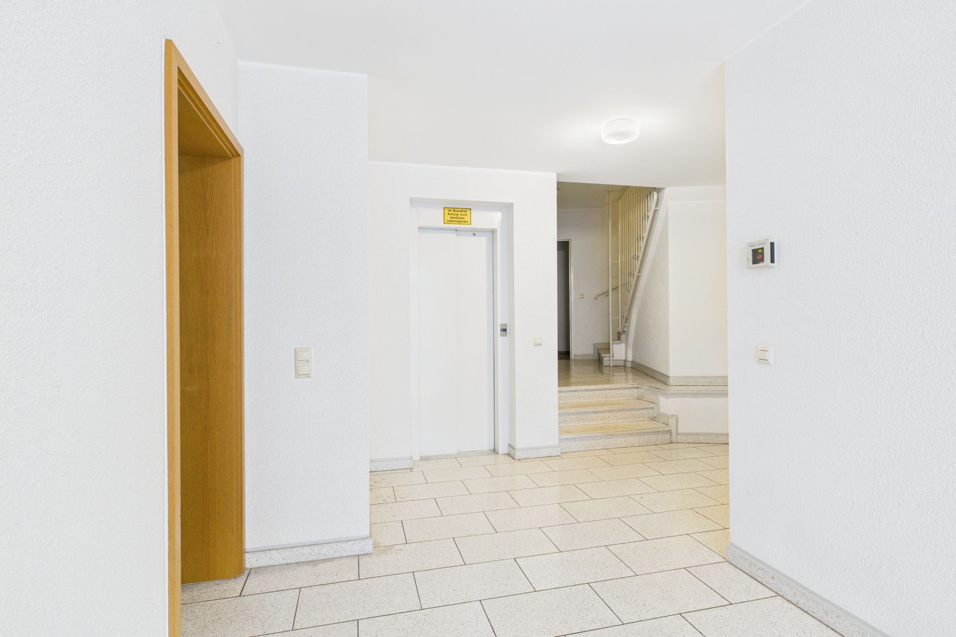 Heller Flur mit Aufzug, Treppe und weißen Wänden in einem Wohnhaus.