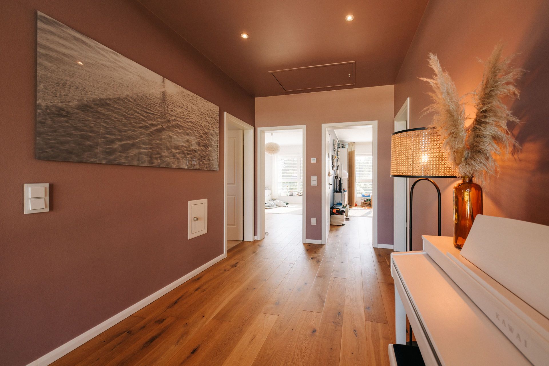 Flur mit Holzfußboden, braunen Wänden, Dekolampe und Bild an der Wand.