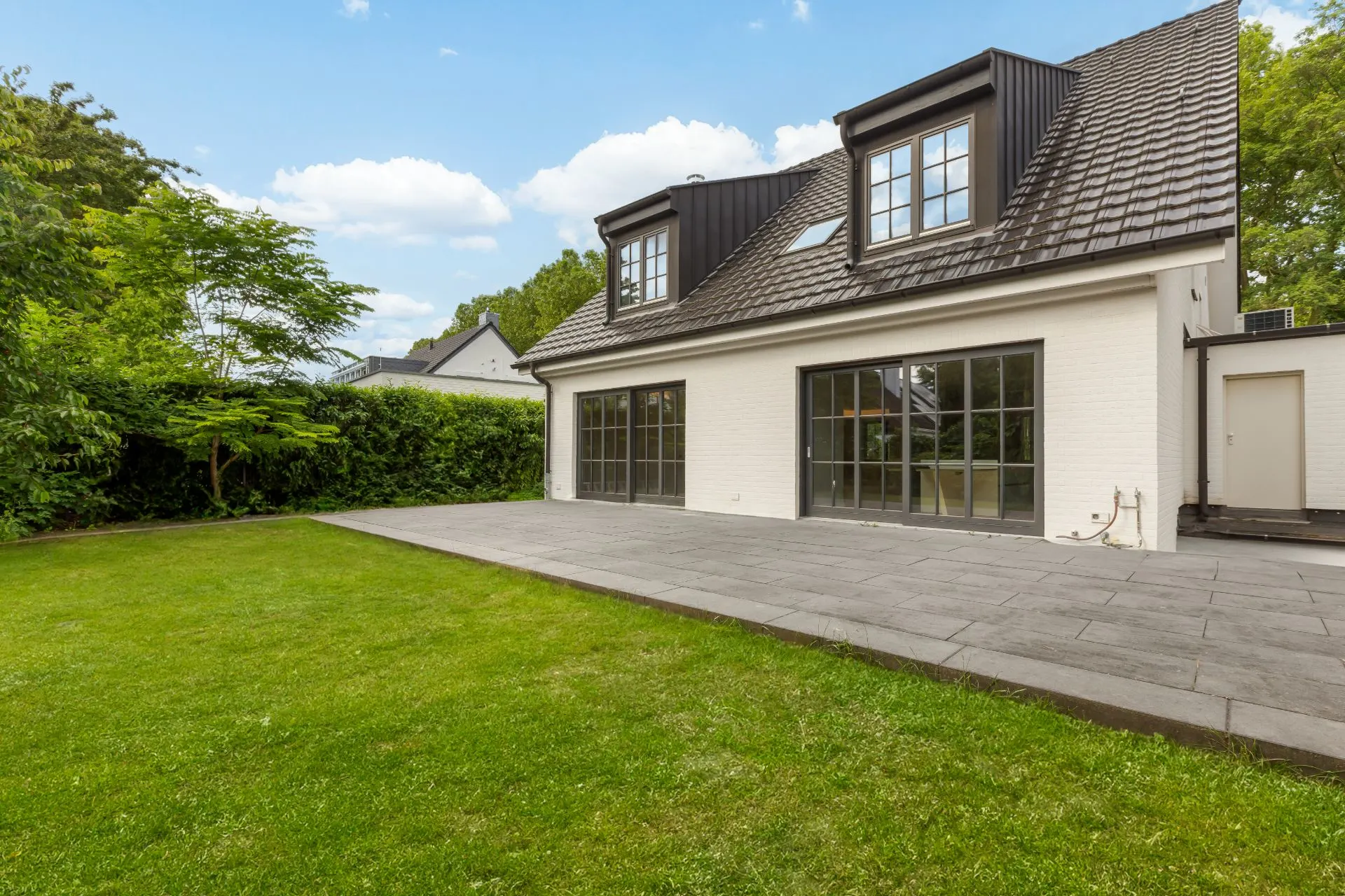 Zweistöckiges Haus mit großen Fenstern, Terrasse und gepflegtem Rasen im Garten.
