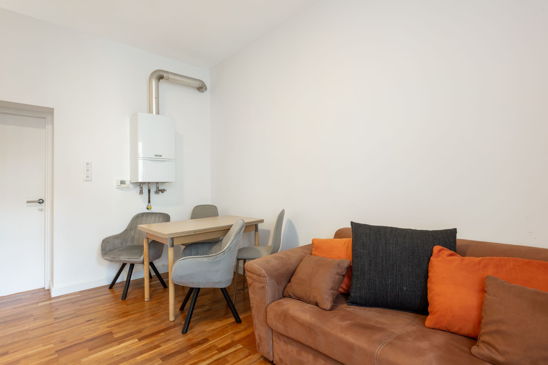 Wohnzimmer mit braunem Sofa, Esstisch mit vier Stühlen und Wandheizung auf Holzfußboden.