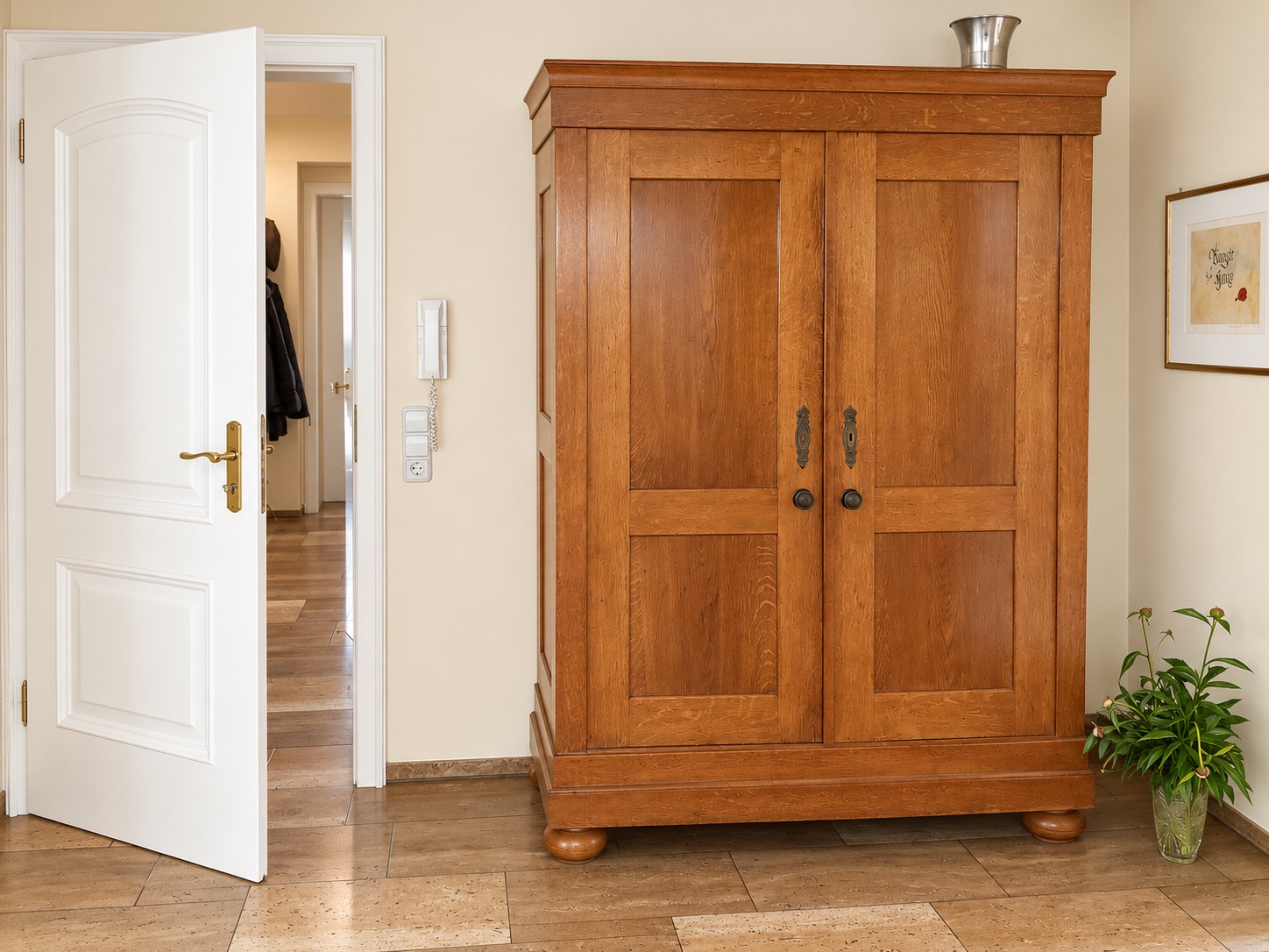 Großer Holzschrank in einem Flur mit geöffneter weißer Tür und Topfpflanze daneben.