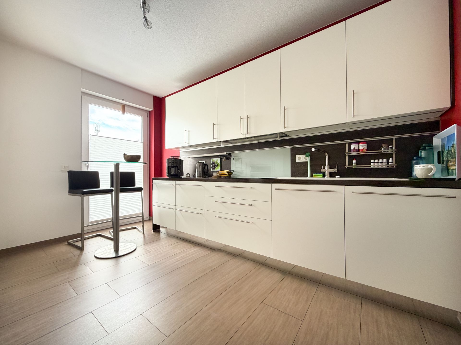 Moderne Küche mit weißen Schränken, Fenster und kleinem Bartisch mit zwei Stühlen.
