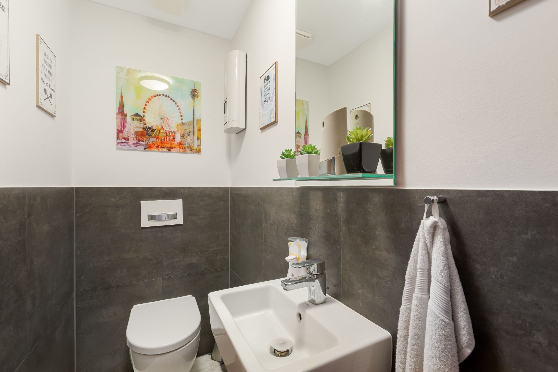 Kleines Badezimmer mit Toilette, Waschbecken, Spiegel und Pflanzen auf einem Glasregal.