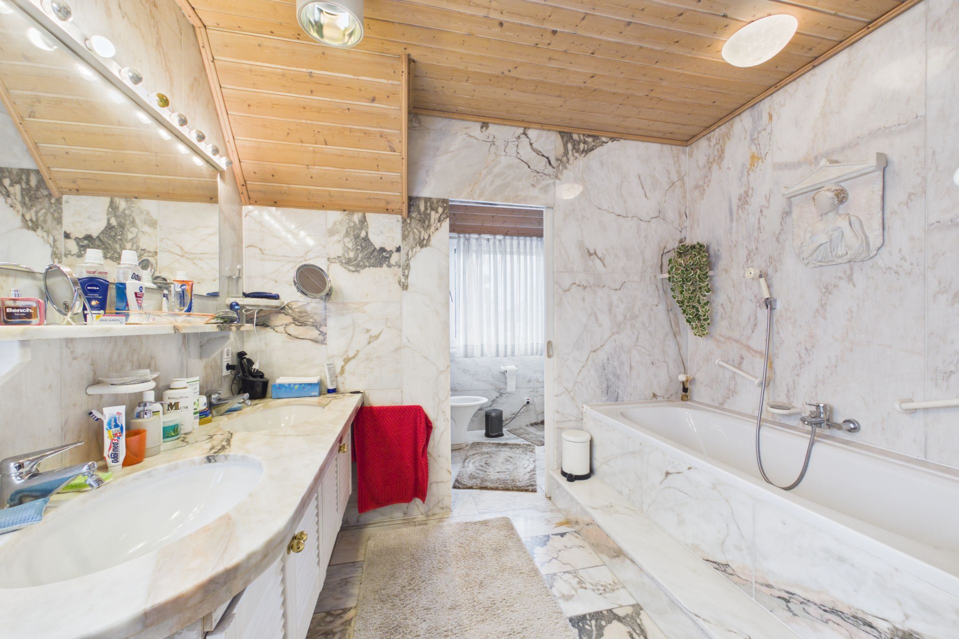 Marmorbad mit Doppelwaschbecken, Badewanne und Holzdecke, rotes Handtuch neben dem Waschbecken.