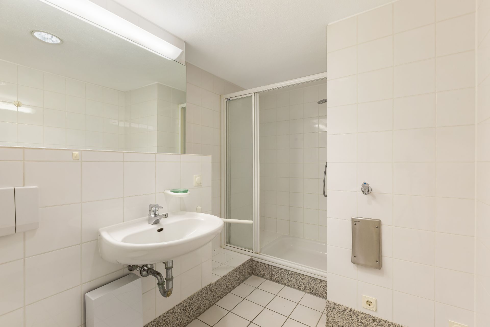 Helles Badezimmer mit Waschbecken, Spiegel und einer Dusche mit Glastür.