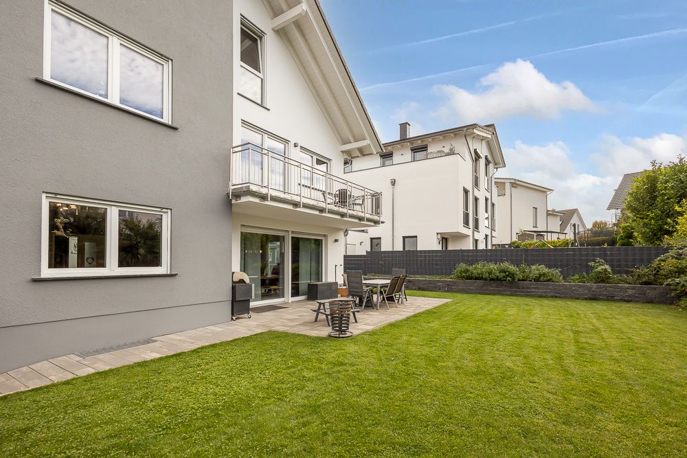 Garten mit Terrasse und Sitzmöbeln neben einem modernen Wohnhaus.