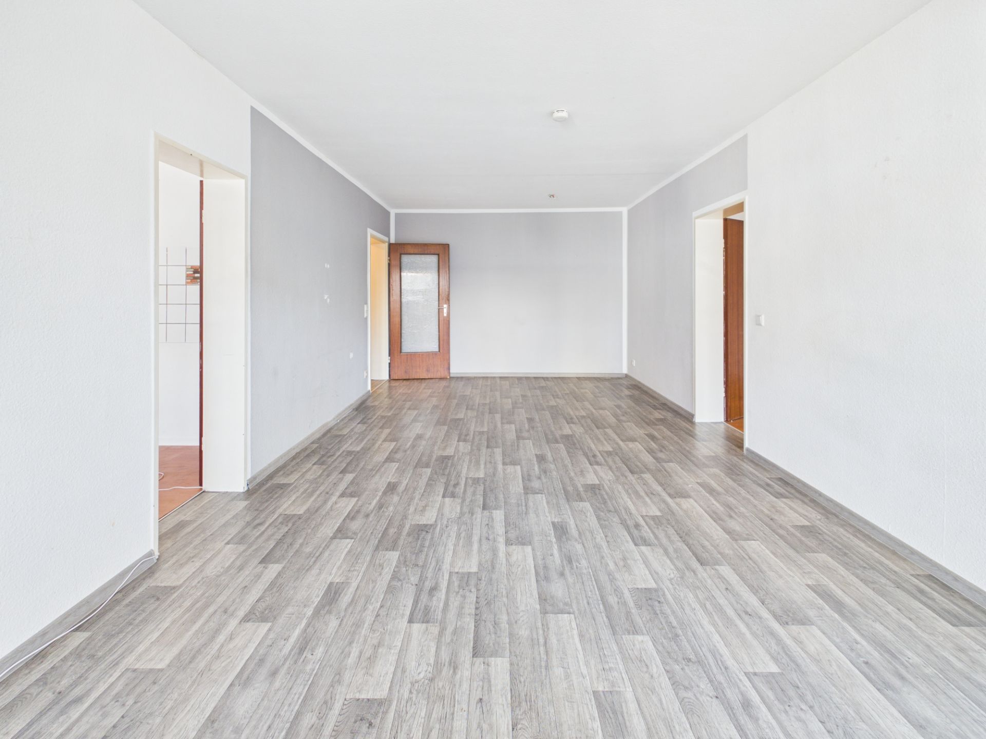 Heller, leerer Raum mit grauem Holzfußboden und mehreren offenen Türen.