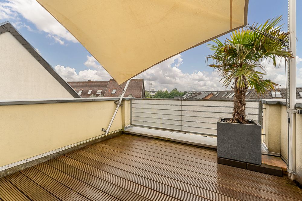 Balkon mit Holzfußboden, Sonnensegel und Palme im großen Pflanzkübel.