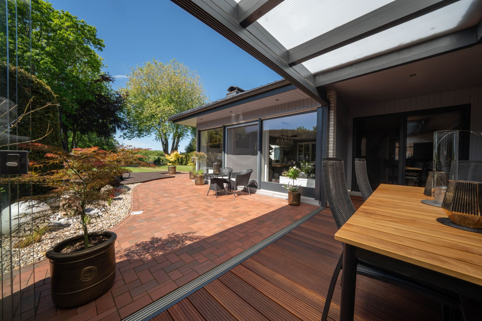 Terrasse mit Holztisch, Stühlen und Blick auf einen Garten mit Bäumen und Pflanzen.