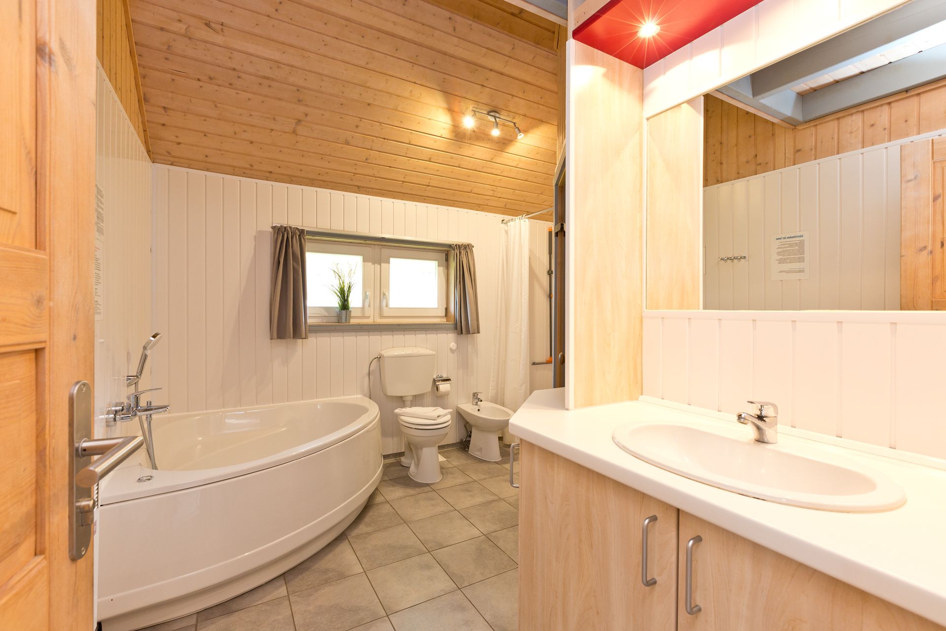 Helles Badezimmer mit Badewanne, Waschbecken, WC und Fenster mit Vorhängen.