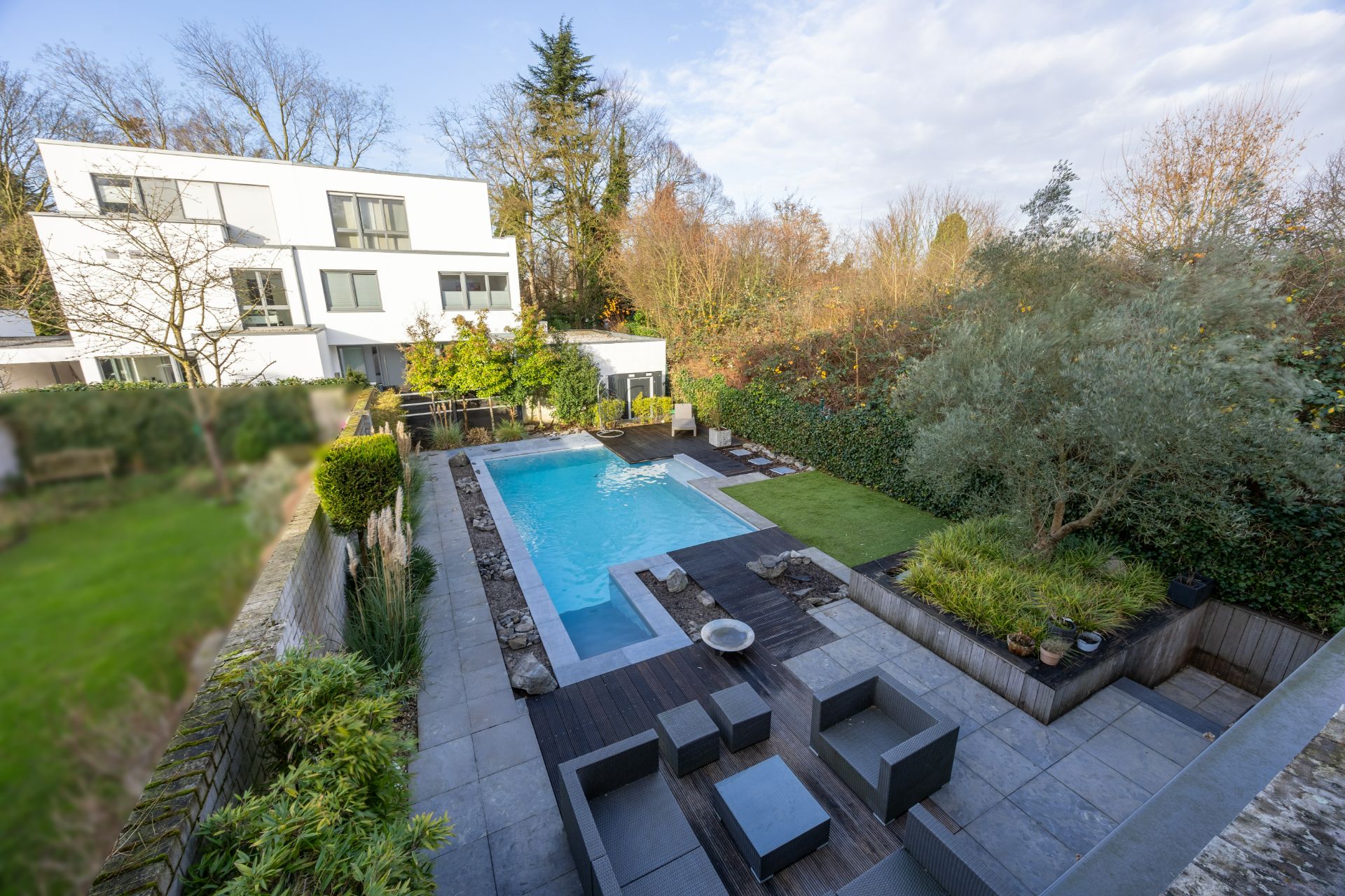 Moderner Garten mit Pool, Sitzbereich und Rasen hinter einem weißen Wohnhaus.