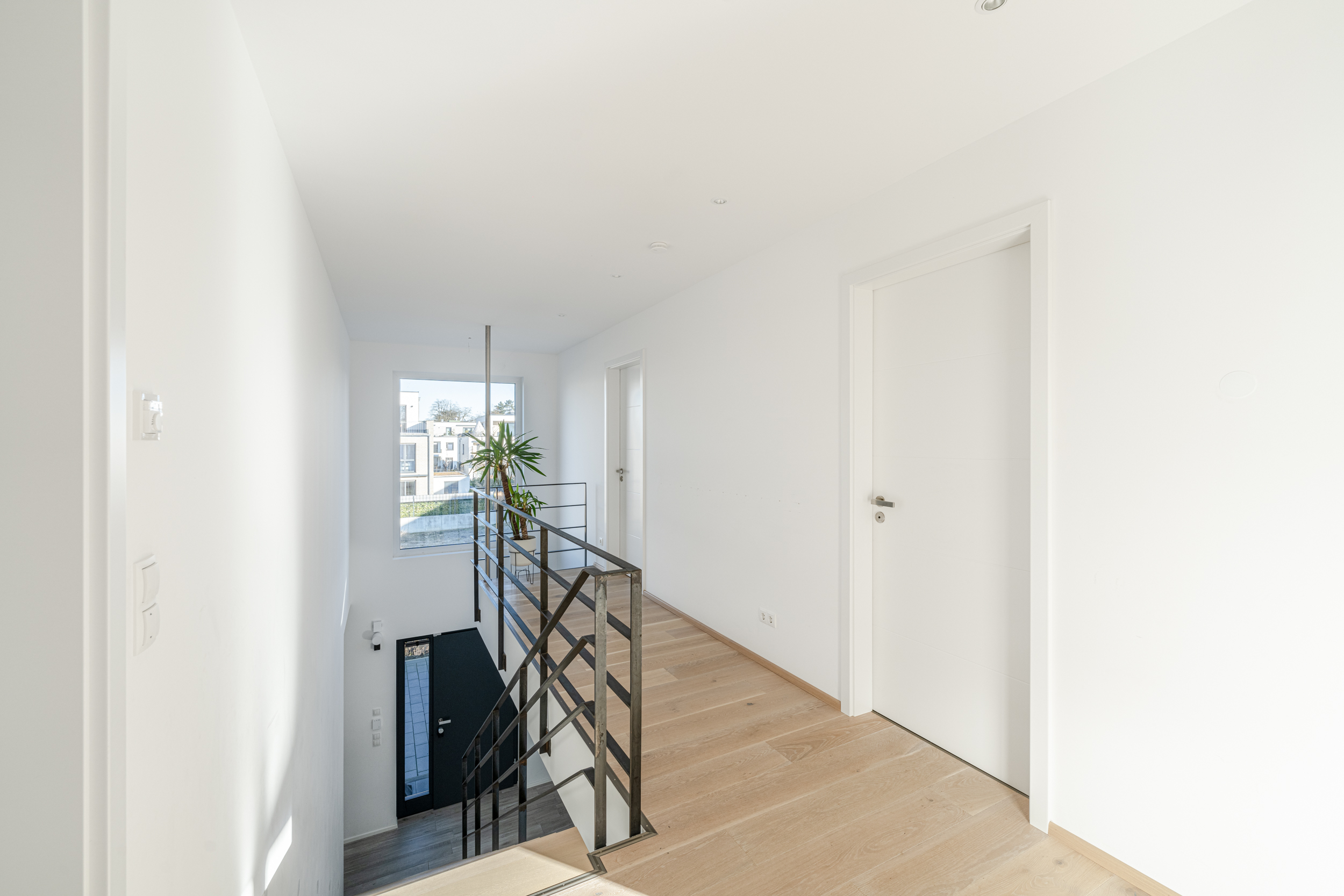 Heller Flur mit Holzfußboden, Treppe und großem Fenster, Zimmerpflanze am Ende.