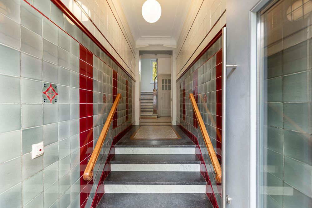 Eingangsflur mit gefliesten Wänden, Handläufen und Treppe in einem Wohnhaus.