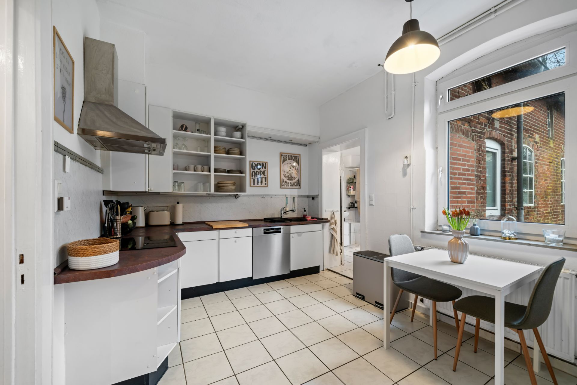 Moderne, helle Küche mit Esstisch, Stühlen, großen Fenstern und offenen Regalen.