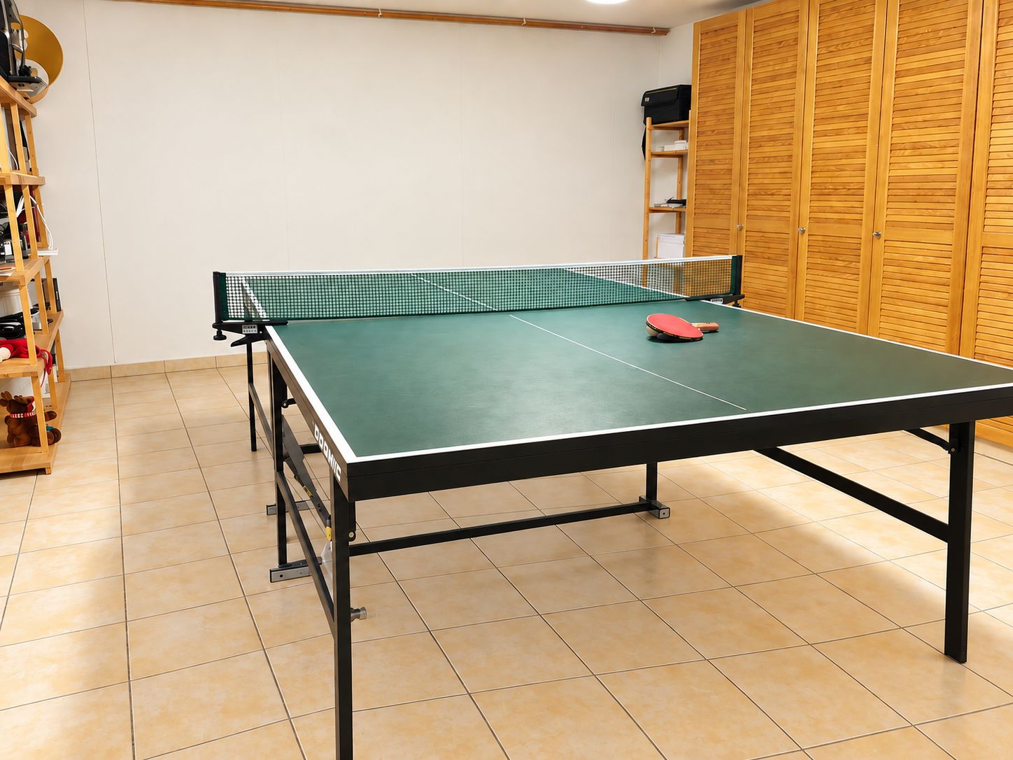 Ein Raum mit Tischtennisplatte, Schläger und Aufbewahrungsregalen.
