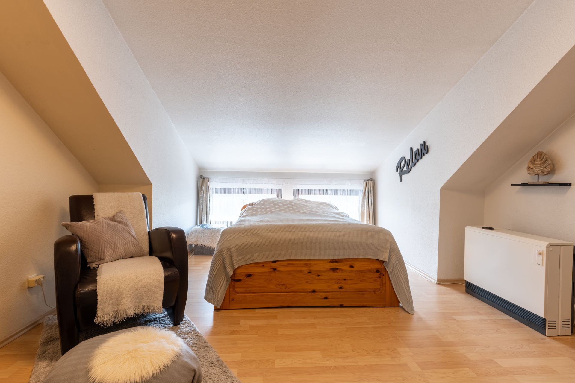 Schlafzimmer mit Doppelbett, Sessel und hellen Fenstern unter Dachschrägen.