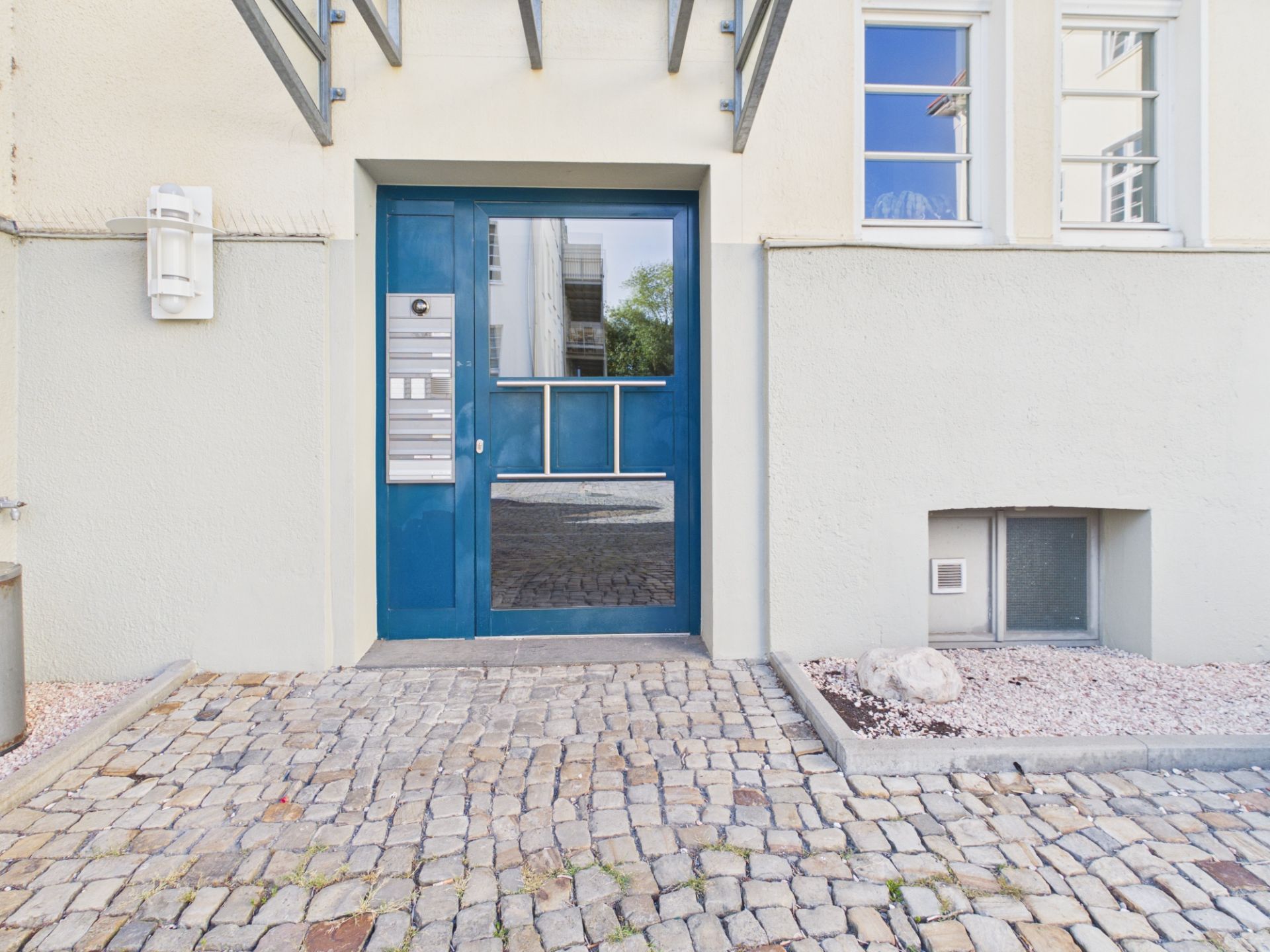 Blaue Hauseingangstür mit Klingelanlage, Fenstern und Kopfsteinpflaster davor.