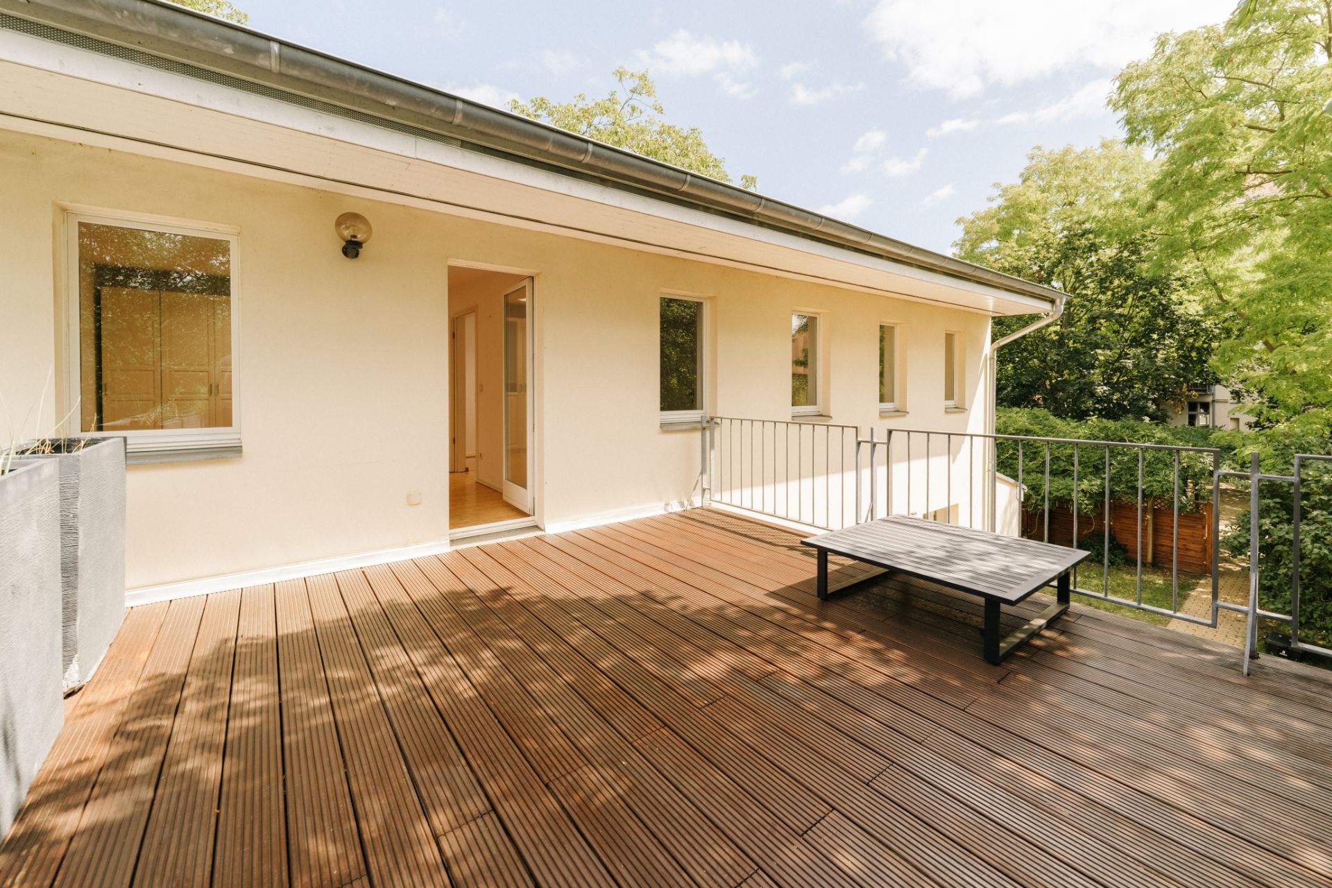 Große Holzterrasse mit Geländer, Bank und Blick auf Bäume, Zugang zum Haus durch Glastür.