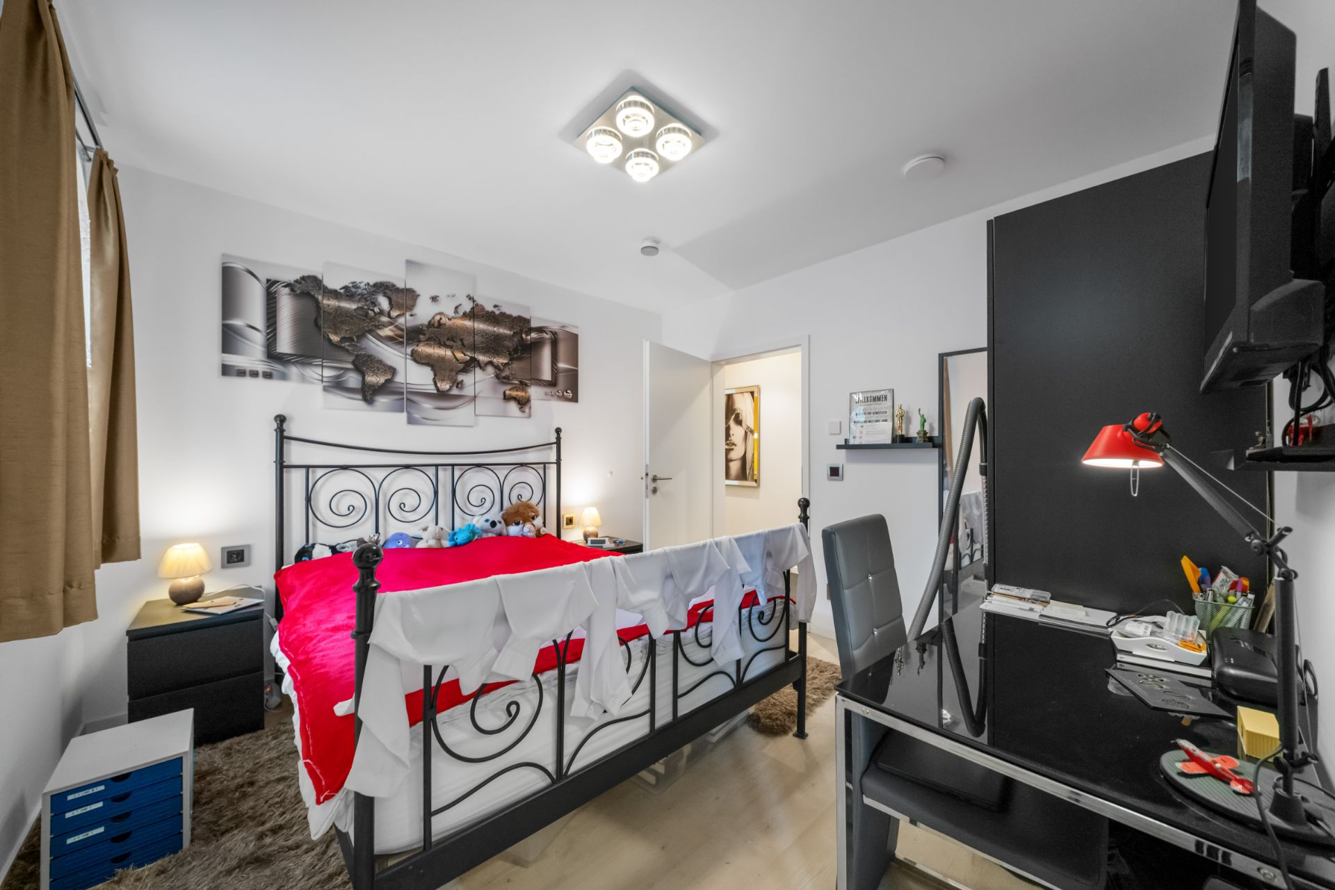Helles Schlafzimmer mit schwarzem Metallbett, Schreibtisch und Wandbildkarte.