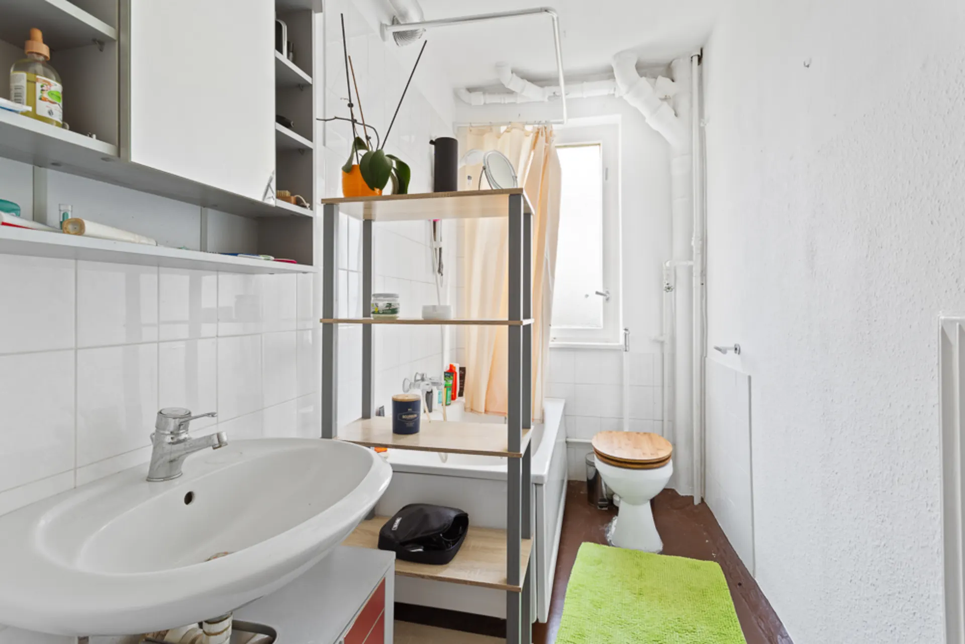 Helles Badezimmer mit Waschbecken, Badewanne, Regal, WC und grünem Teppich.
