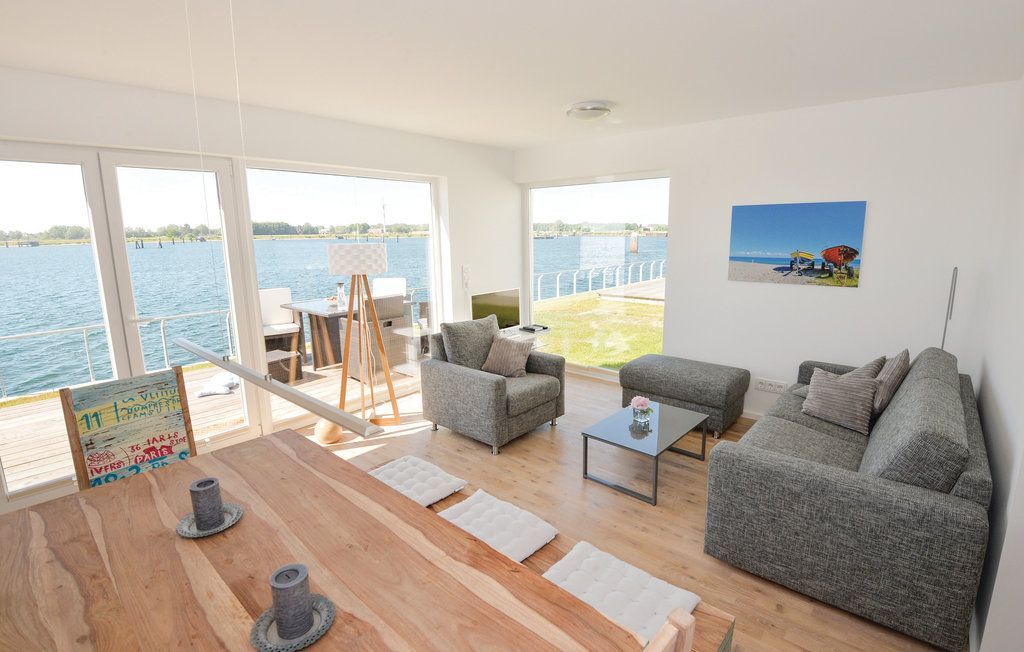 Helles Wohnzimmer mit Seeausblick, zwei grauen Sofas, Holztisch und Terrasse.