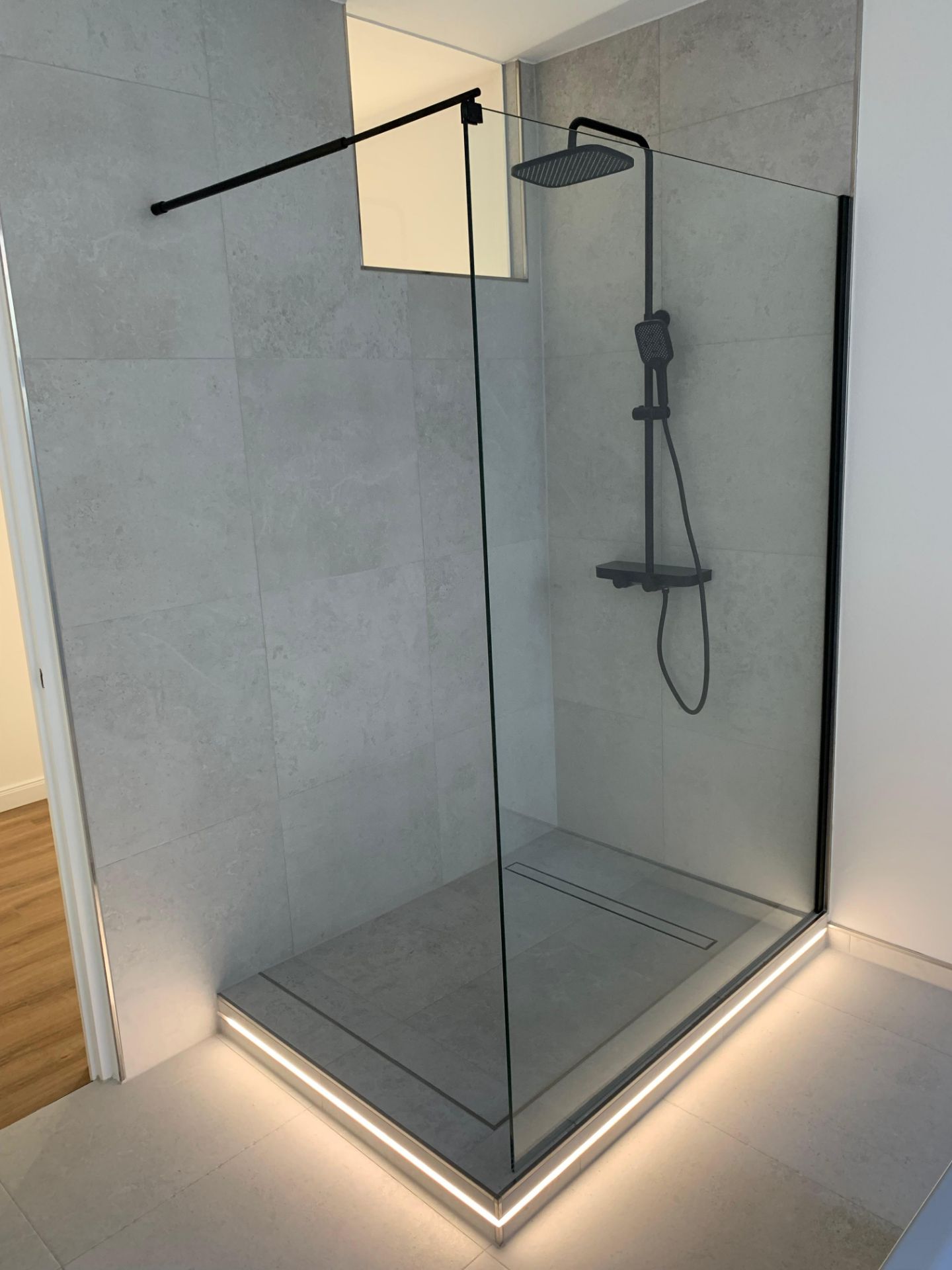 Moderne, offene Dusche mit Glaswänden und schwarzer Armatur, mit Beleuchtung am Duschboden.