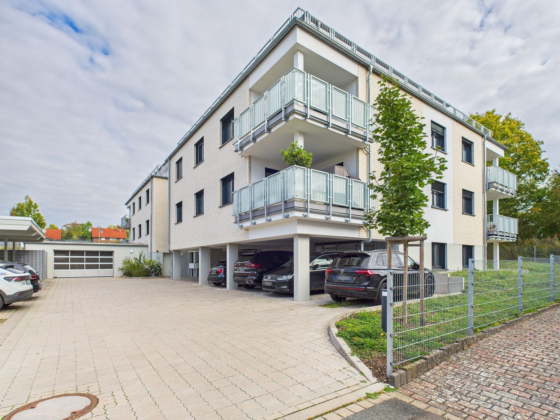 Modernes Wohngebäude mit Balkonen, Tiefgaragenstellplätzen und parkenden Autos davor.