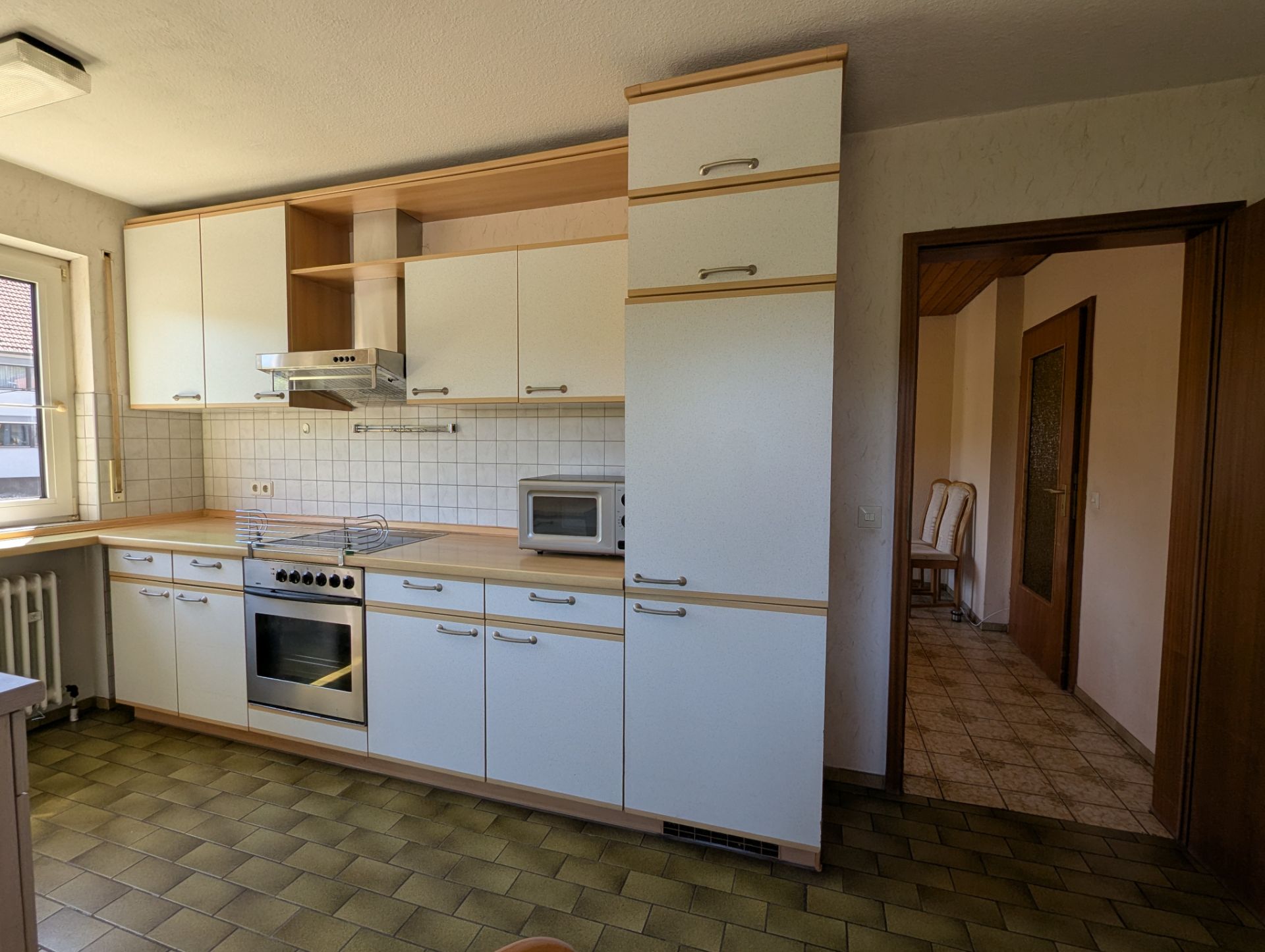 Helle Küche mit weißen Schränken, Backofen, Herdplatte, Mikrowelle und Fenster.