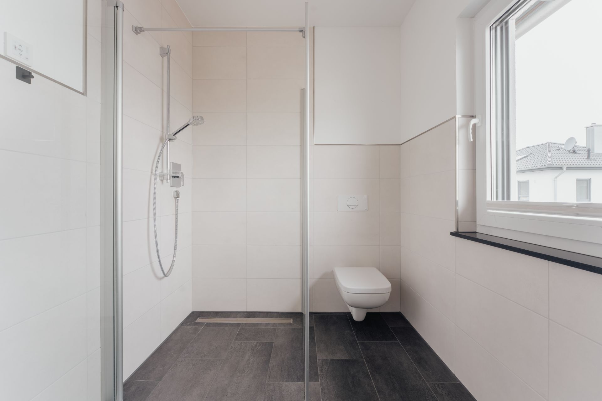 Modernes Bad mit bodengleicher Dusche, Hänge-WC und großem Fenster.