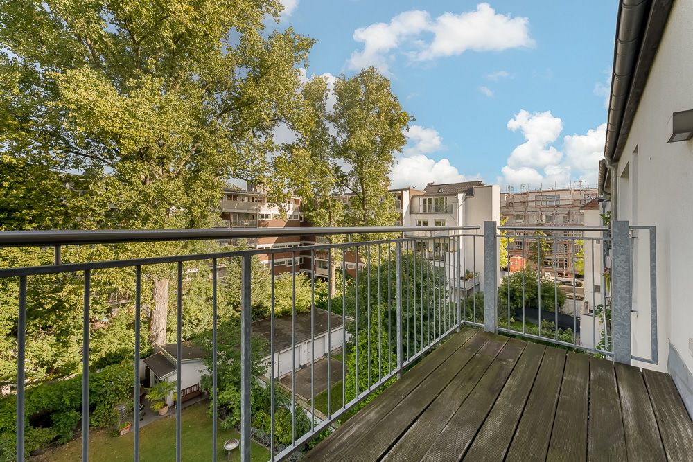 Balkon mit Holzfußboden und Metallgeländer, Blick auf Bäume und benachbarte Wohngebäude.