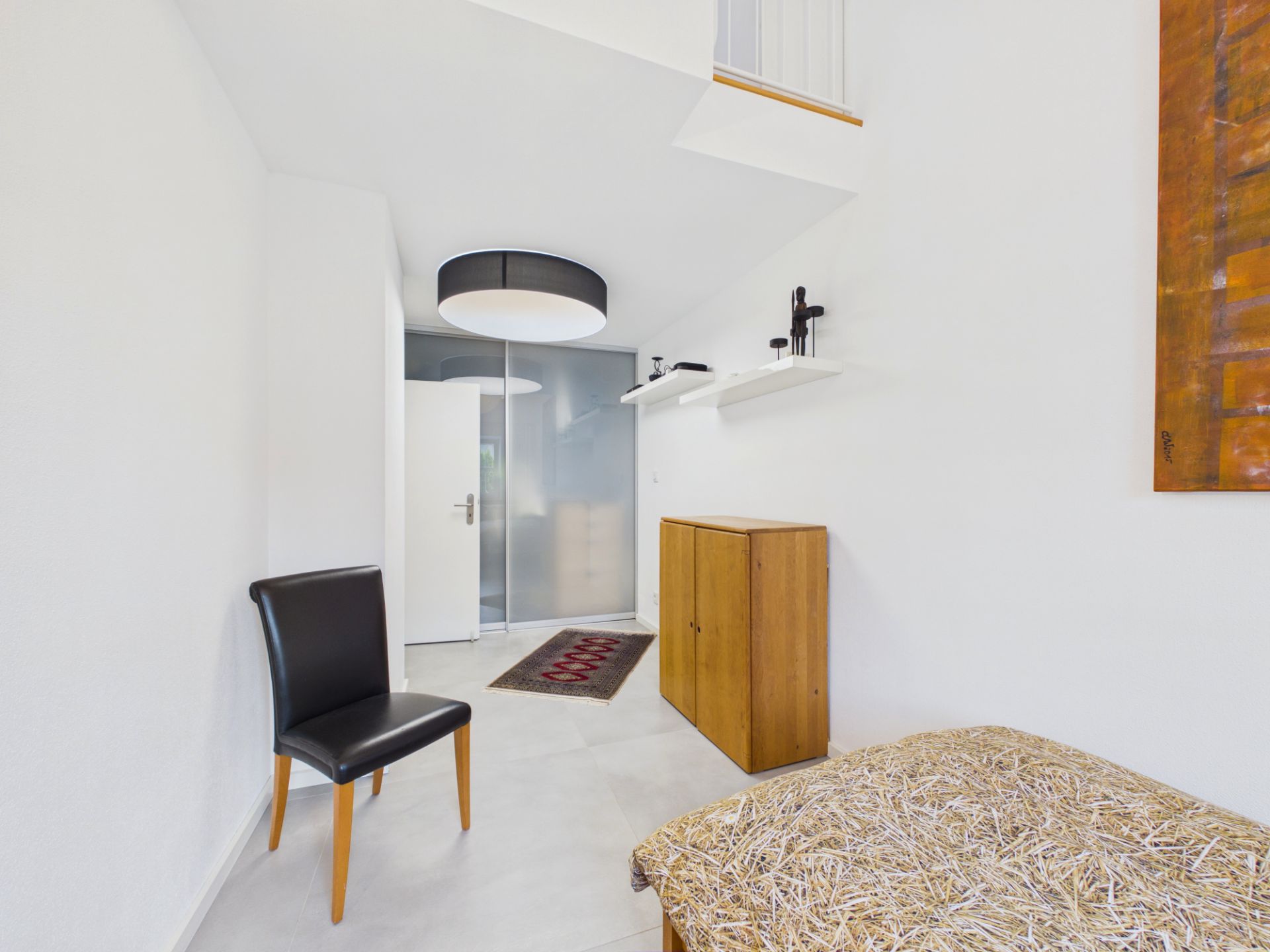 Heller Flur mit schwarzem Stuhl, Holzkommode, Wandregalen und moderner Deckenleuchte.