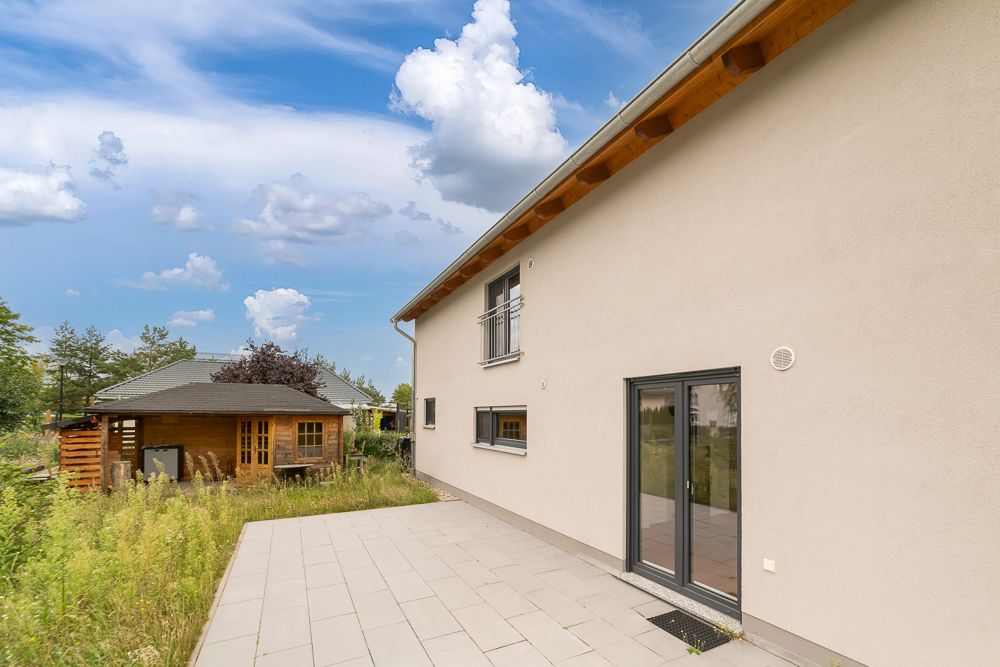 Terrasse eines Wohnhauses mit Fliesenboden, im Hintergrund ein Gartenhaus und Bewuchs.