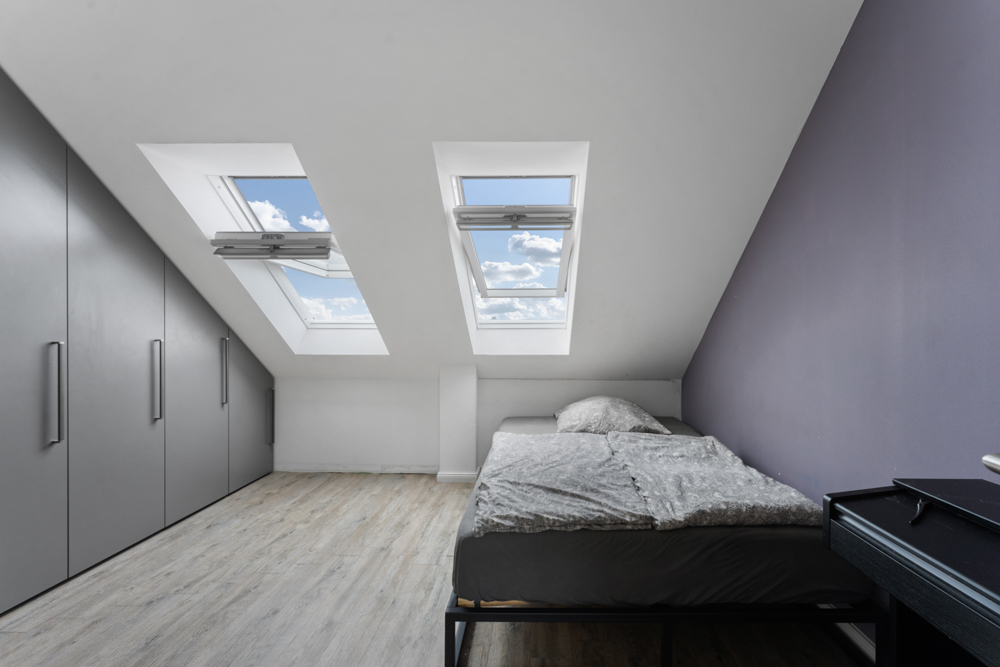 Modernes Schlafzimmer mit Dachschrägen, zwei Dachfenstern und grauem Schrank.