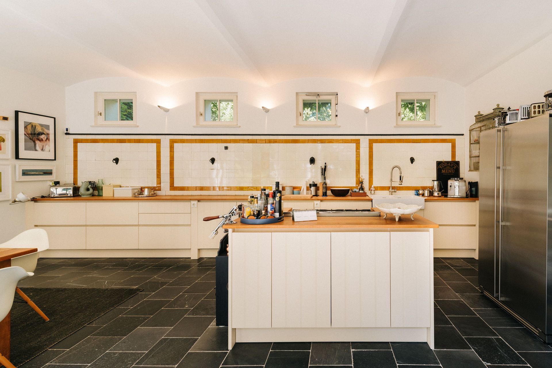 Helle Küche mit Kücheninsel, weißen Schränken, gelben Fliesen und großem Kühlschrank.