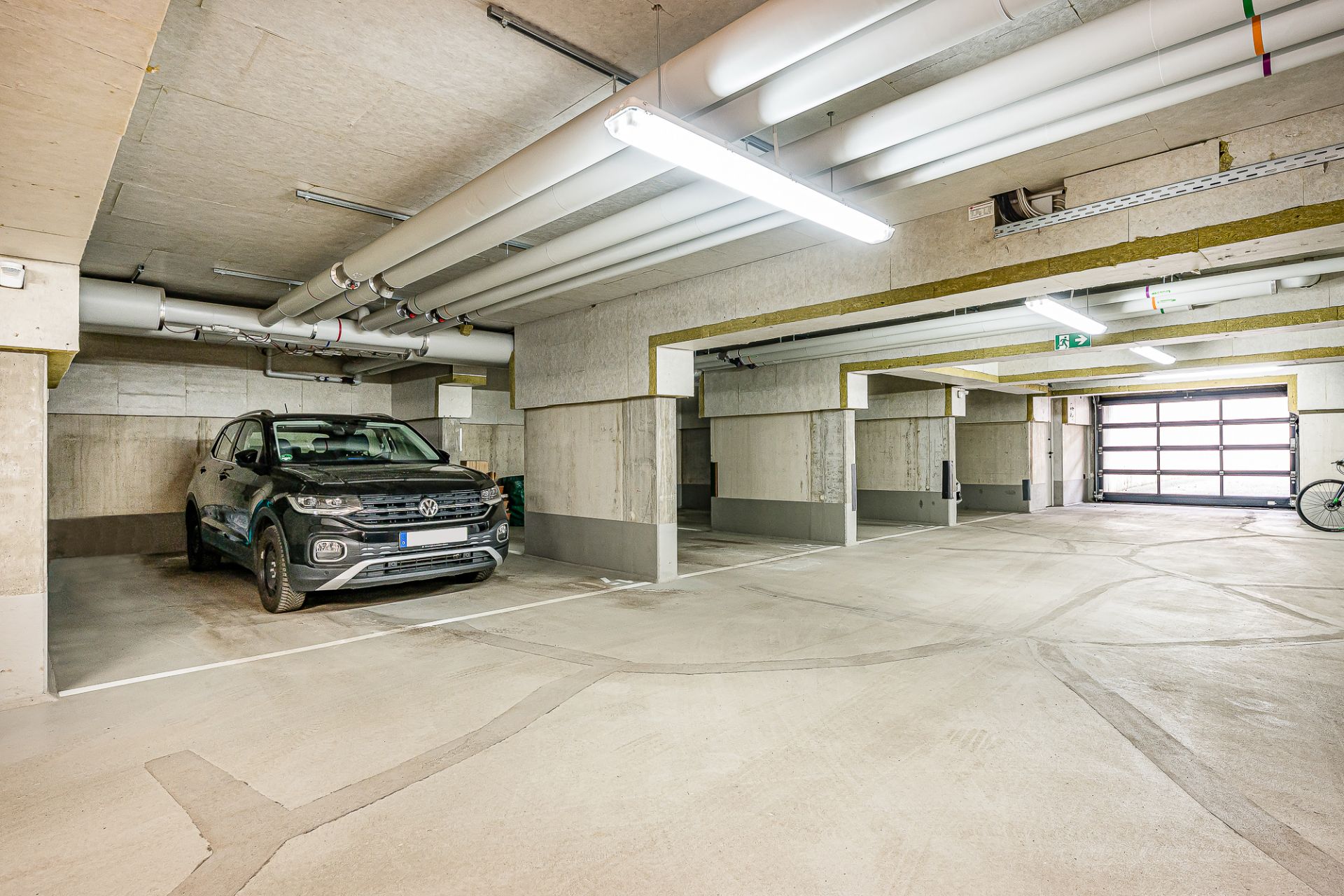 Tiefgarage mit geparktem Auto, Fahrrad und Betonsäulen.