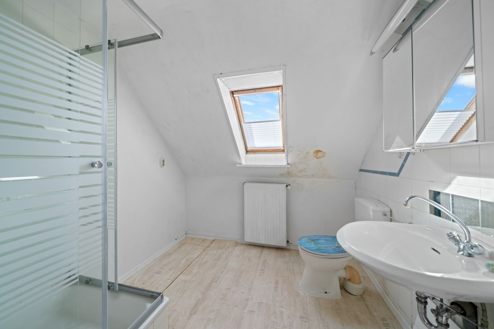 Helles Badezimmer mit Dachschräge, Dusche, Toilette, Waschbecken und Fenster.