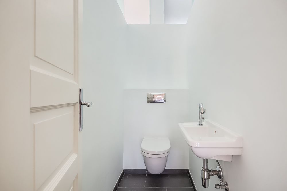 Kleines, weißes Badezimmer mit wandhängender Toilette und kleinem Waschbecken.