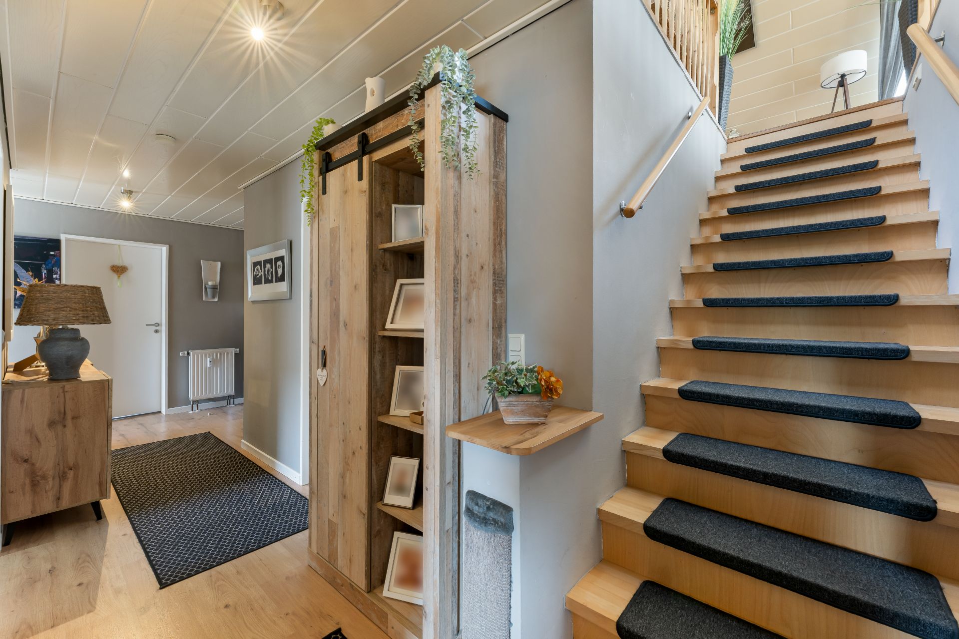 Hausflur mit Holztreppe, Regal, Kommode und Dekorationen, helle Wände und Teppichläufer.