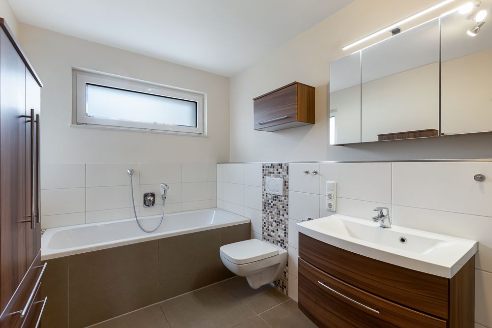 Modernes Badezimmer mit Badewanne, Waschbecken, Wandspiegel, WC und Holzschränken.