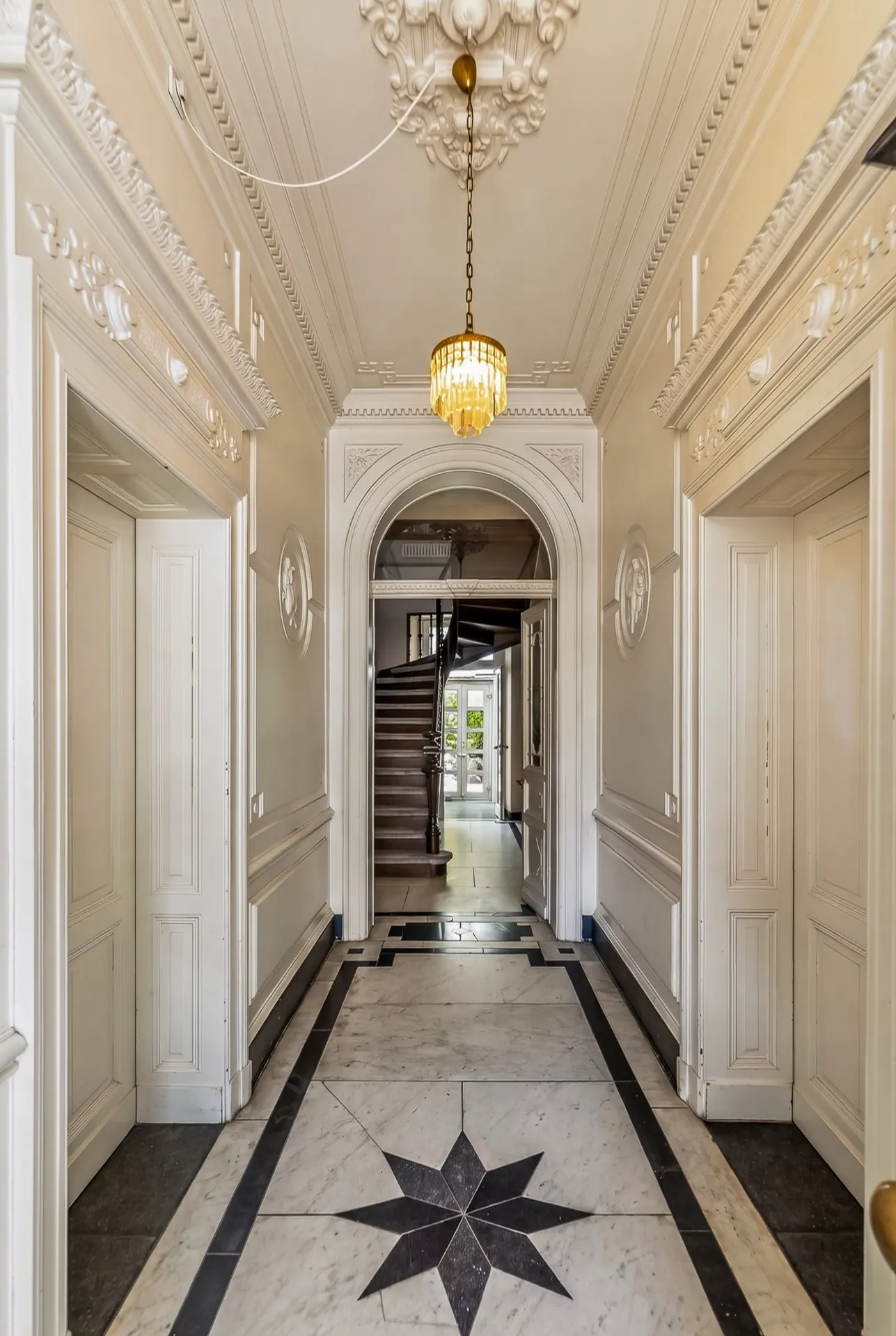 Eleganter Flur mit Marmorboden, Kronleuchter und Treppe im Hintergrund.