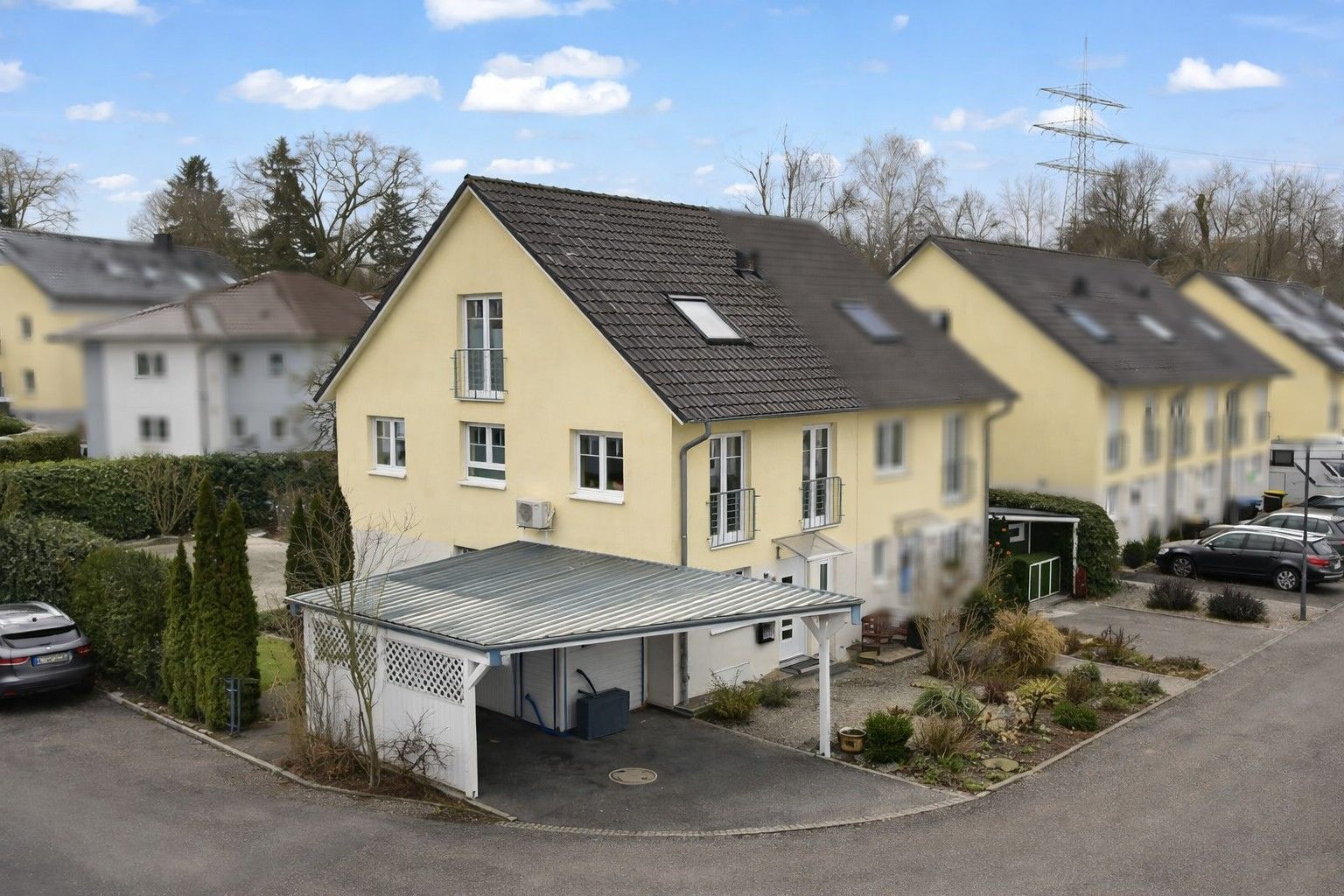 Doppelhaushälfte mit gelber Fassade, Carport und kleinem Garten davor.